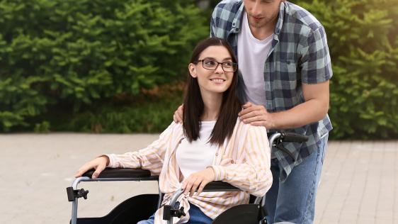 Ein Mann ist mit einer Frau im Rollstuhl unterwegs.