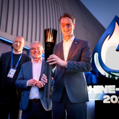 NRW-Ministerpräsident Hendrik Wüst trägt beim Head of Delegation Dinner die FISU-Fackel in den Mülheimer Luftschiffhangar.