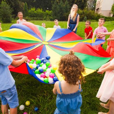 Kinder stehen im Kreis und spielen mit einem bunten Tuch und Bällen