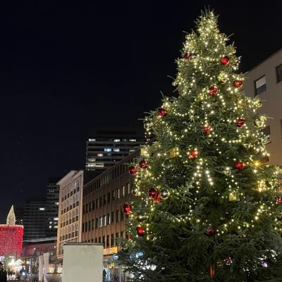 Weihnachtsbaumdekoriert mit Kugeln und Lichterketten und im Hintergrund ist ein Weihnachtsmarkt