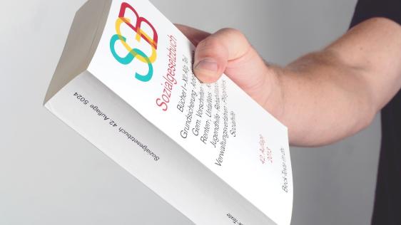 Person hält das Sozialgesetzbuch - SGB - in der Hand. Leistungsgewährung, Hilfebedürftige, Soziales, Sozialagentur
