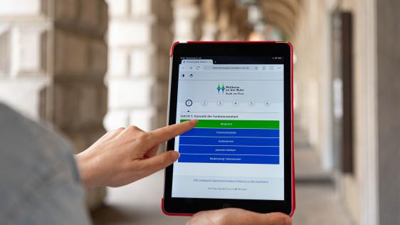 Auf dem Tablet wird das Serviceportal aufgerufen, im Hintergrund ist das Rathaus zu sehen.