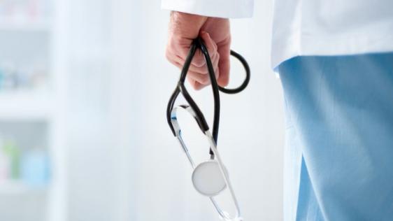 Die Rückseite eines Arztes im Flur eines Krankenhauses. Er hält ein Stethoskop in der Hand.
