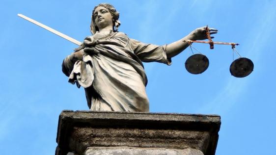Justicia-Statue mit Waage und Schwert in den Händen, im Hintergrund blauer Himmel. Gerechtigkeit, Rechtsgrundlagen, gesetzlichen Grundlagen