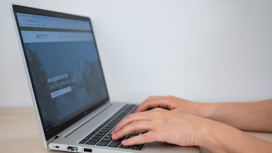 Hände tippen auf Laptop-Tastatur mit geöffneter Webseite der Stadt Mülheim an der Ruhr