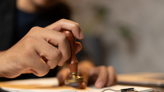 Hand einer Person hält einen Stempel über Unterlagen auf einem Clipboard, um diese zu Beurkunden. Urkundenservice, Siegel
