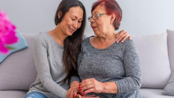 Zwei Frauen sitzen nebeneinander, eine hält die Hand der anderen, unterstützt und tröstet sie. Beratungsangebote, Betreuungsangebote, Unterstützung, Hilfestellung