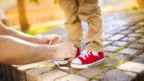Erwachsener bindet einem Kind die Schuhe. 
