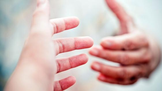 Eine Hand nähert sich einer anderen Hand um Hilfe anzubieten