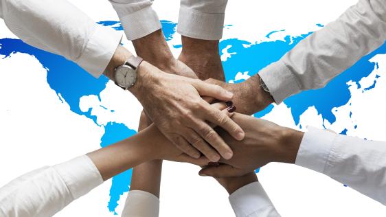 Übereinanderliegene Hände vor einer Weltkarte, die die internationale Zusammenarbeit symbolisieren