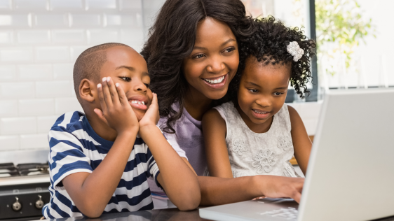 Mutter mit Kindern sitzt am Laptop und lacht.