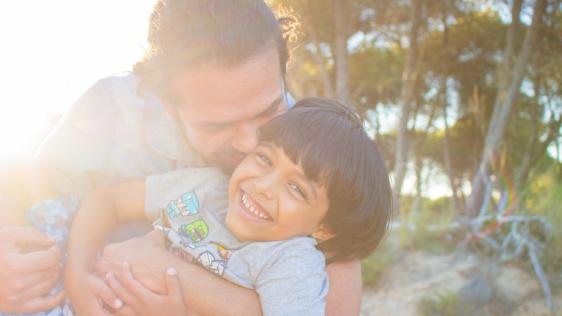Junger Vater hält seinen Sohn auf dem Arm und gibt ihm einen Kuss. Eltern, Alleinerziehende, Adoption, Tagespflege, Pflegekinder