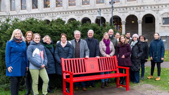 Das Foto zeigt die neue Bank gegen Gewalt an Frauen am Tag der Einweihung am 29.11.2023 durch den Oberbürgermeister Marc Buchholz, den Vorstandsvorsitzenden der Sparkasse Martin Weck und die Vertreter*innen der Gleichstellungsstelle und des Runden Tisches gegen häusliche Gewalt.