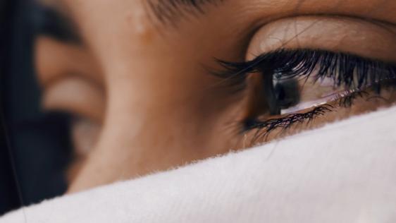 Bildausschnitt, tränengefüllte Augen einer Frau, mit weißem Tuch vor Mund und Nase.  