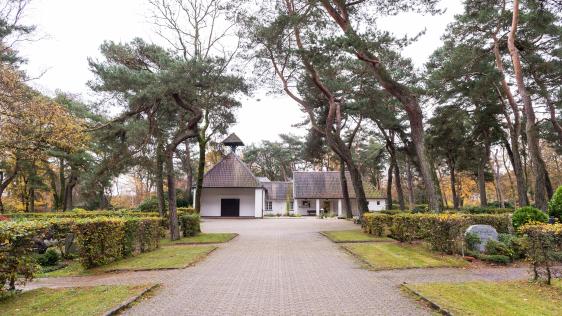 Blick auf die Trauerhalle in Speldorf. Rechts und links des Weges Grasstreifen und Hecken.