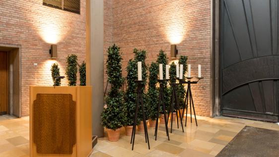 Trauerhalle innen Hauptfriedhof. Kanzel mit Bäumen in Kübeln und Kerzenständer mit weißen Kerzen
