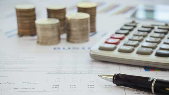 Stapel Münzen, Taschenrechner und Kugelschreiber auf Finanzdokument mit Zahlen und Tabellen