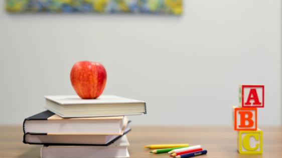 Roter Apfel auf vier Büchern, daneben liegen Stifte