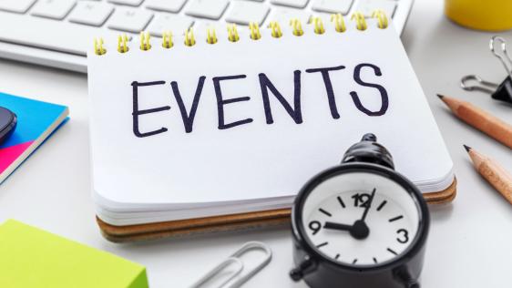 Auf einem Schreibtisch liegt ein Notizblock mit dem Wort "Events". Daneben befinden sich Stifte und eine Tastatur.