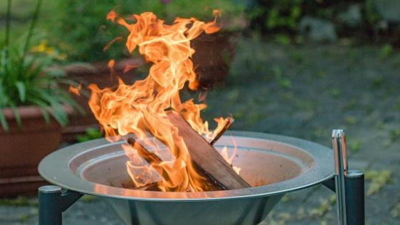 Eine brennende Feuerschale, im Hintergrund ist ein Garten zu sehen.