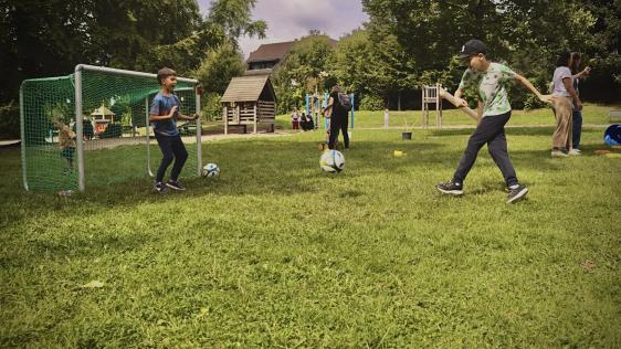 Drei Kinder spielen Fußball auf einer Wiese.