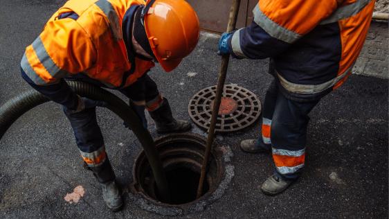 Zwei Kanalarbeiter, die Wasser in einen Kanalschacht einleiten.