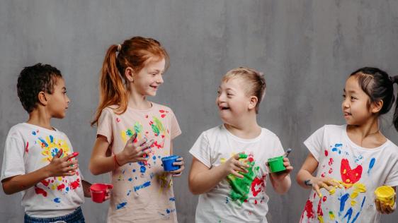 Zwei Jungs und zwei Mädchen mit Farbspritzer auf dem Shirt stehen lachend zusammen.