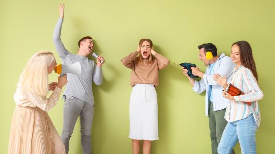 Fünf Personen auf einem Bild. Die mittlere hält sich die Ohren zu, wohingegen je zwei Personen links und rechts verschiedensten Lärm verursachen.