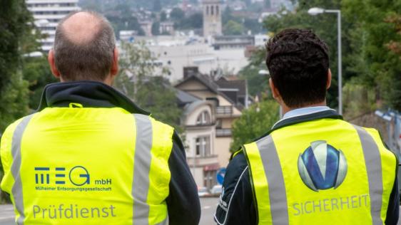 Rückansicht auf zwei Mitarbeitende der Mülheimer Entsorgungsgesellschaft (MEG) in Signalwesten mit Blick auf die Stadt..