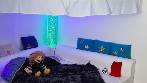 Eine Kuschelecke mit einer Lavalampe, Kissen und einer Decke lädt zum Entspannen ein.