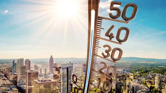 Ein Thermometer zeigt eine hohe Temperatur um die 40 Grad an. Im Hintergrund liegt eine Stadt bei schönem Wetter.