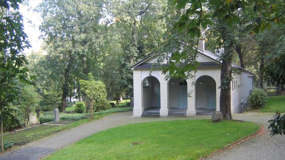 Trauerhalle auf dem Altstadtfriedhof. Den Hintergrund bilden grün belaubte Bäume, einzelne historische Grabmale sind zu erkennen