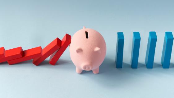 blaue und rote Dominosteine die an einem Sparschwein abprallen