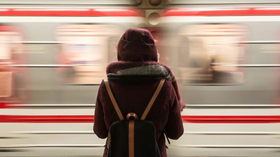 Eine Person am Bahnsteig blickt in Richtung eines vorbeifahrenden Zuges.
