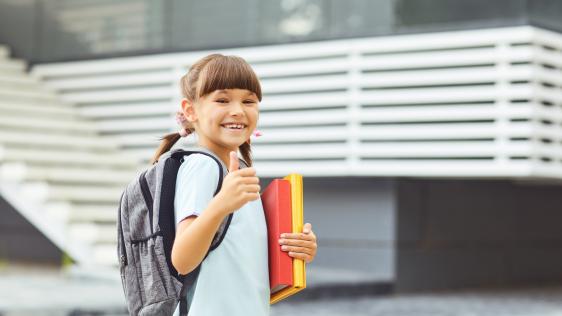 Mädchen steht glücklich vor einer Schule 