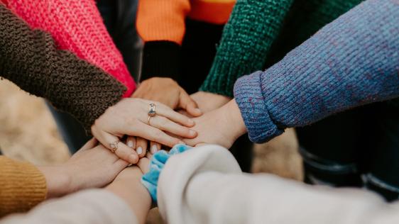 eine Gruppe von Frauen die Ihre Hände aufeinander legen. Das Bild steht Symbolisch für Zusammenhalt unter Frauen.