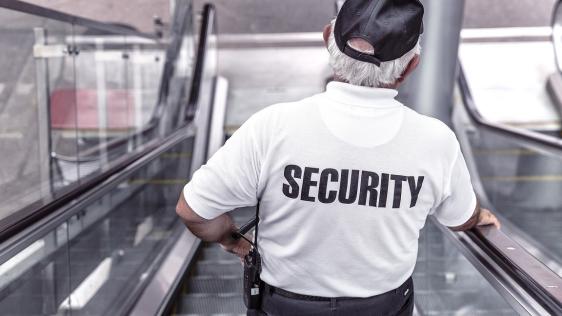 Wachmann mit der Aufschrift Security auf dem Rücken auf einer Rolltreppe