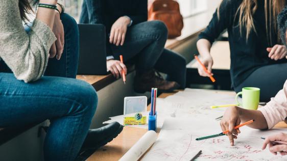 Bildausschnitt, Studierende sitzen bequem um einen Tisch mit einer Skizze und besprechen eine Teamarbeit.
