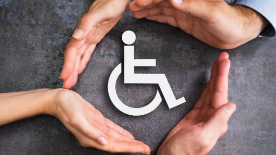 Vier Hände schützen das Symbol eines Rollstuhlfahrers