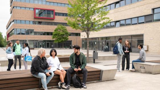 Studenten der HRW sitzen gemeinsam auf einer Bank des Campus'.