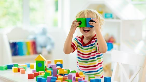 ein Kind, das mit Bauklötzen spielt und sich vors Gesicht hält