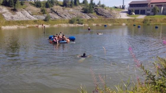 Jugendliche beim Schwimmen und Bootsfahren auf dem kleinen See in der Ferienfreizeit 