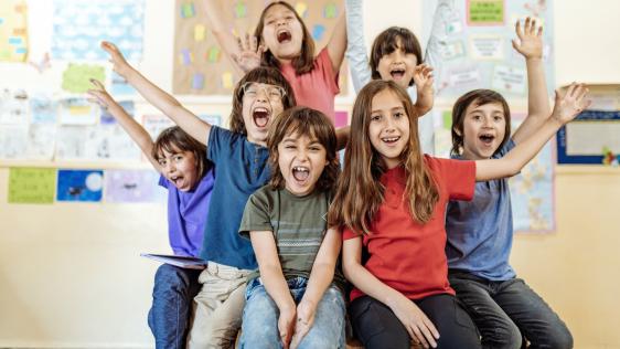 Angehende Schulkinder jubeln, im Hintergrund ein Klassenzimmer.
