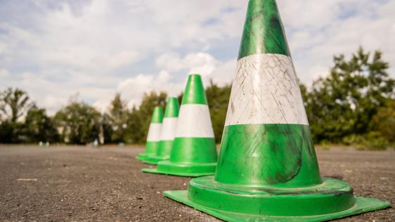 Vier grüne Pylonen in Reihe auf asphaltiertem Grund.