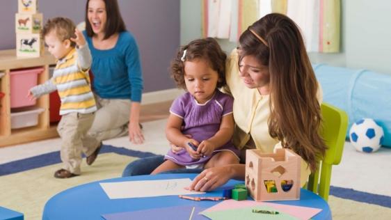 Zwei Kindertagespflegepersonen spielen mit Kleinkindern im Tagespflegenest. 