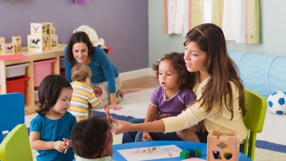 Zwei Tagespflegepersonen spielen mit Kleinkindern im Tagespflegenest. Kindertagespflegepersonen, Kita, Kindergarten, Kinderbetreuung, Pflegevater, Pflegemutter.