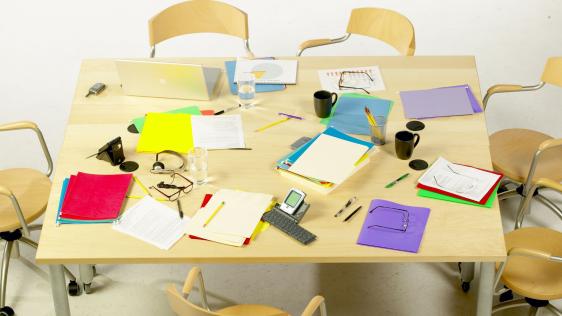 Ein Konferenztisch voller bunter Ordner, Lesebrillen und Schriftstücke.