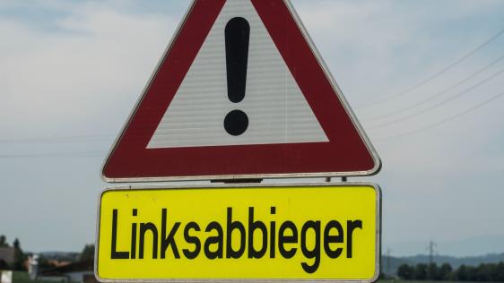 Das Bild zeigt ein Achtung-Schild mit der darunter stehenden Aufschrift "Linksabbieger".