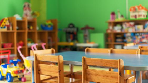Tisch mit Stühlen und im Hintergrund Regale mit Spielsachen 