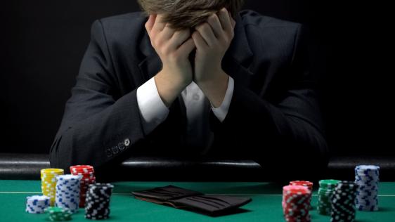 ein Mann der an einem Casino Tisch sitzt und verzweifelt die Hände vor das Gesicht hält
